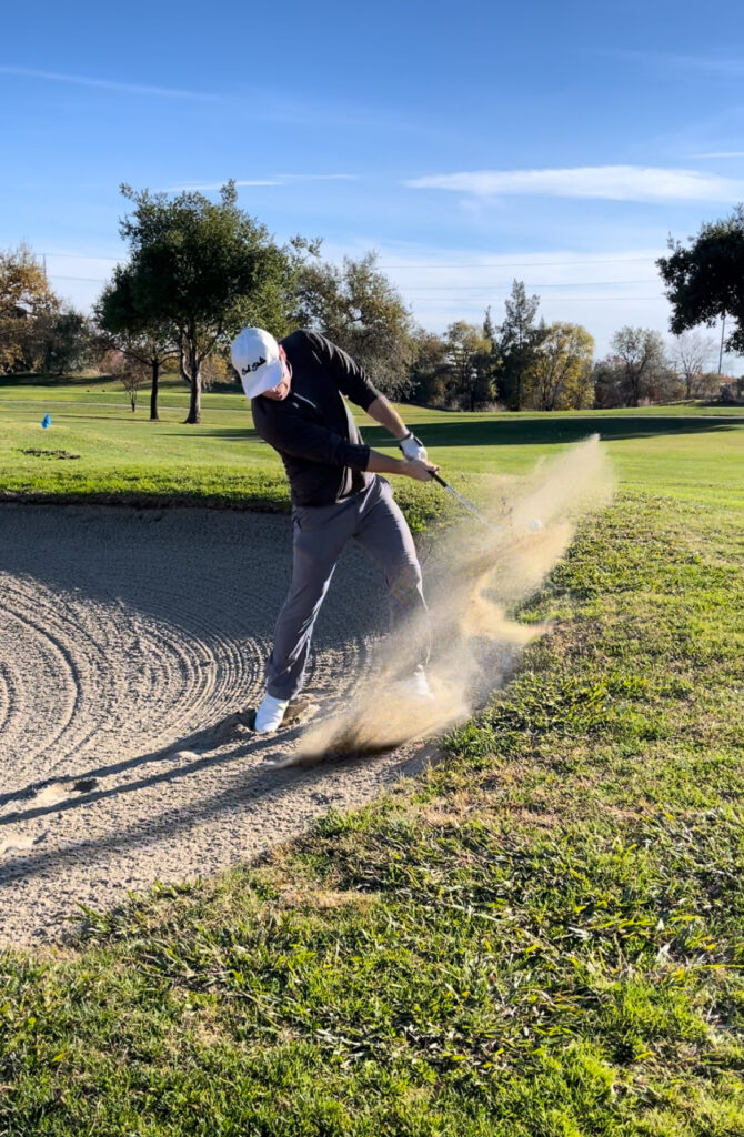 Golfer mid-swing blasting out of a greenside bunker with sand flying in Sacramento region